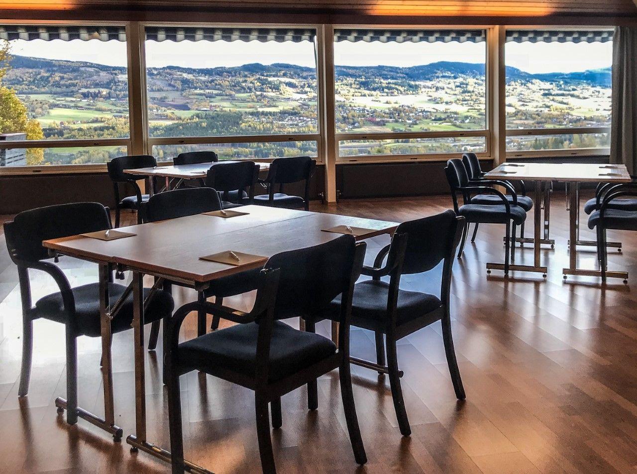 Moderne restaurant med bord og stoler, med utsikt over landskapet gjennom store vinduer.