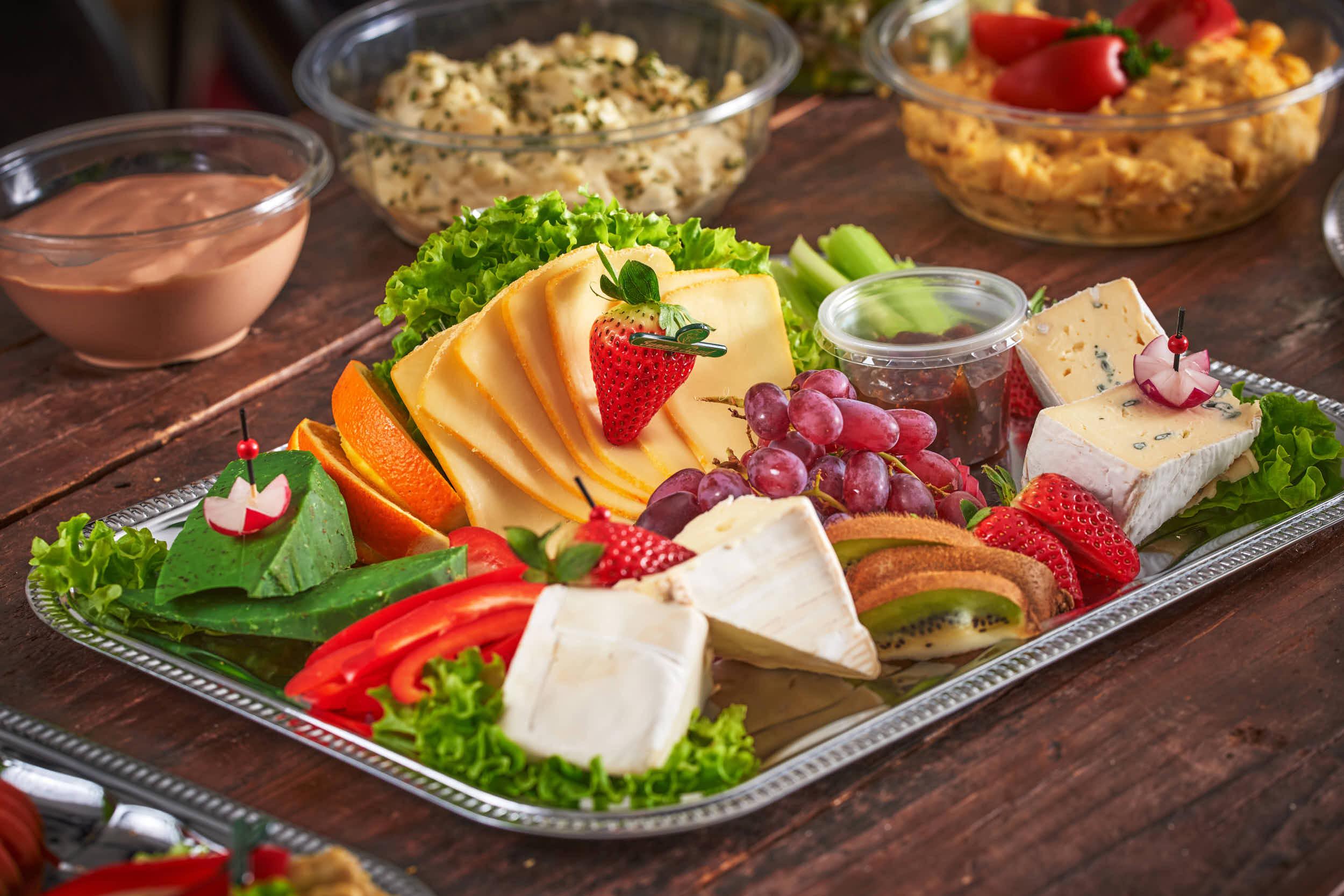 Et fat med assortert frukt og ost, inkludert melon, druer, jordbær, paprika og salat.