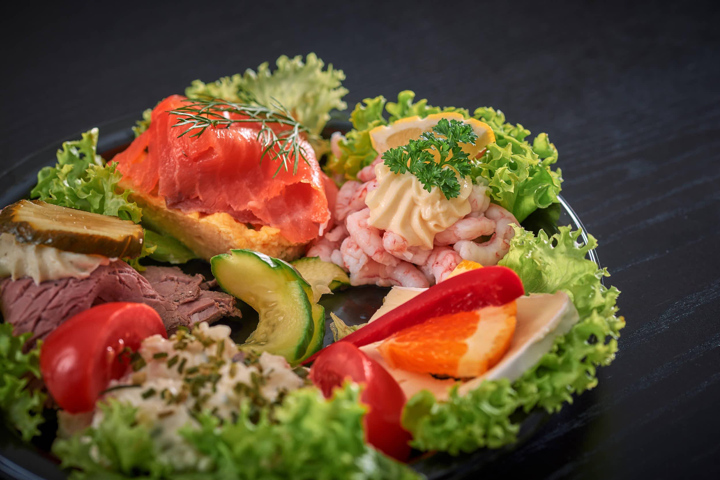 En tallerken med variert kaldmat, inkludert laks, reker, grønnsaker og salat.