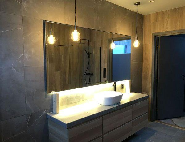 Moderne bad med stor speil, stilige pendellamper og en elegant servant på en trekommode.
