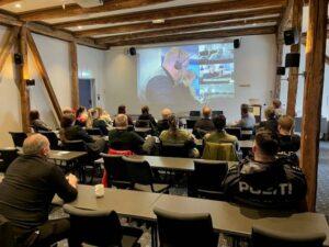 En gruppe mennesker sitter i et møterom og ser på en presentasjon på storskjerm.