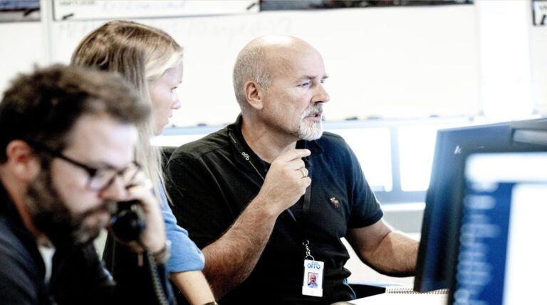 Tre personer jobber sammen på et kontor, med fokus på dataskjermer og telefoner.