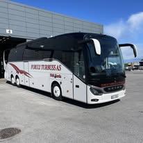 En moderne turistbuss fra Furulund Turbuss AS parkert foran en bygning under en blå himmel.