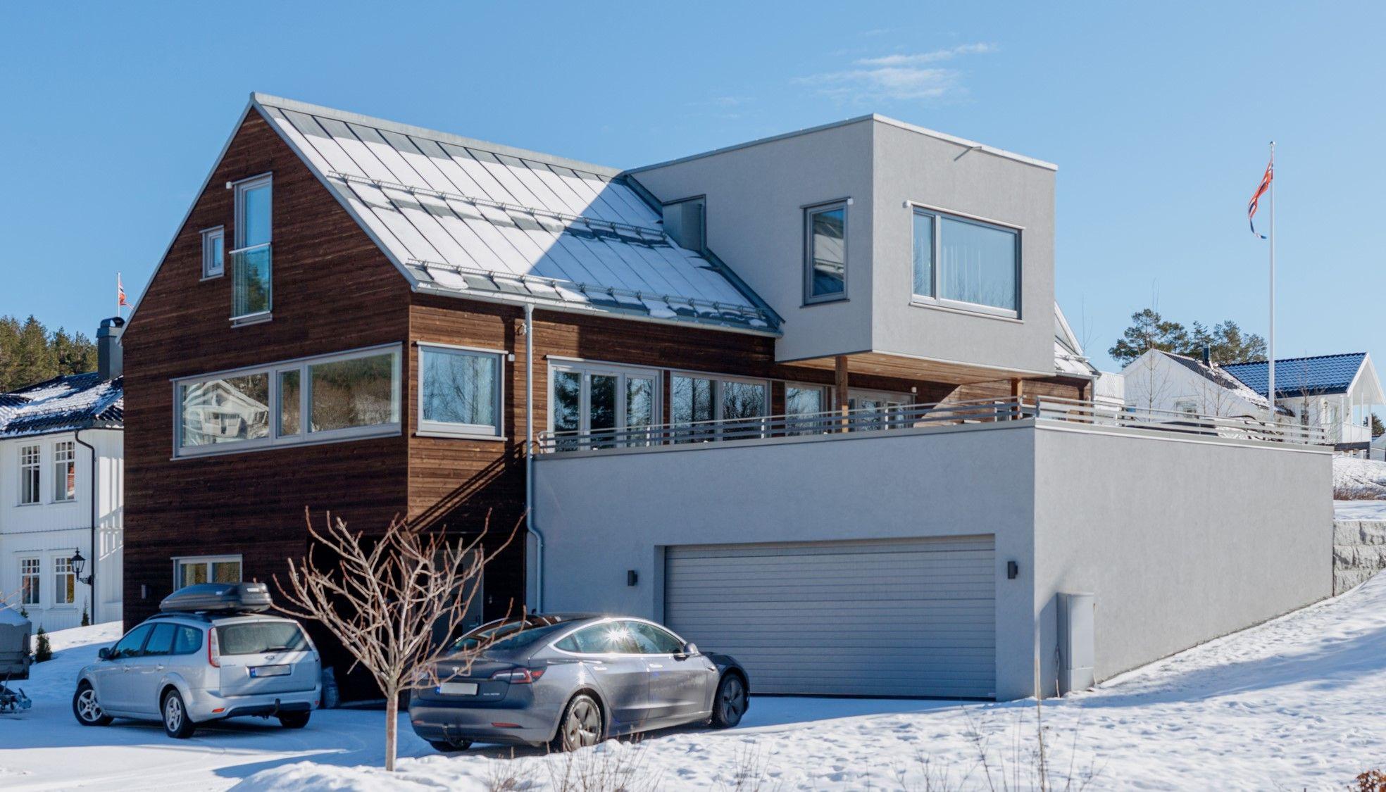 Moderne hus med tre og betong, snødekt hage og biler parkert foran garasje.