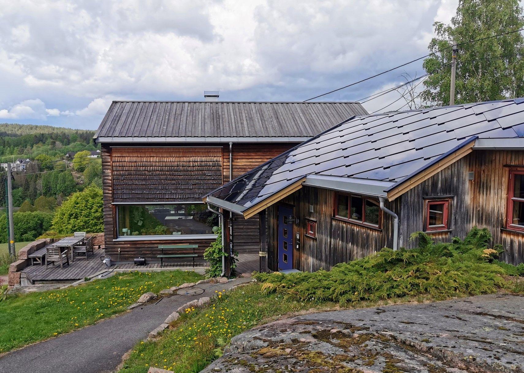 Et koselig hus med solcellepaneler, beliggende i naturskjønne omgivelser med grønt gress og trær.