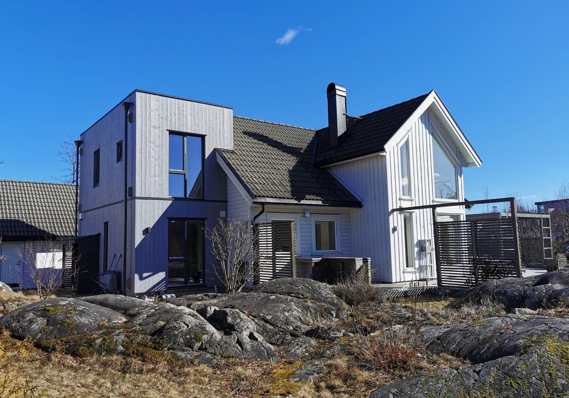 Moderne hus med tre etasjer og store vinduer, plassert på steinete terreng under en klar blå himmel.