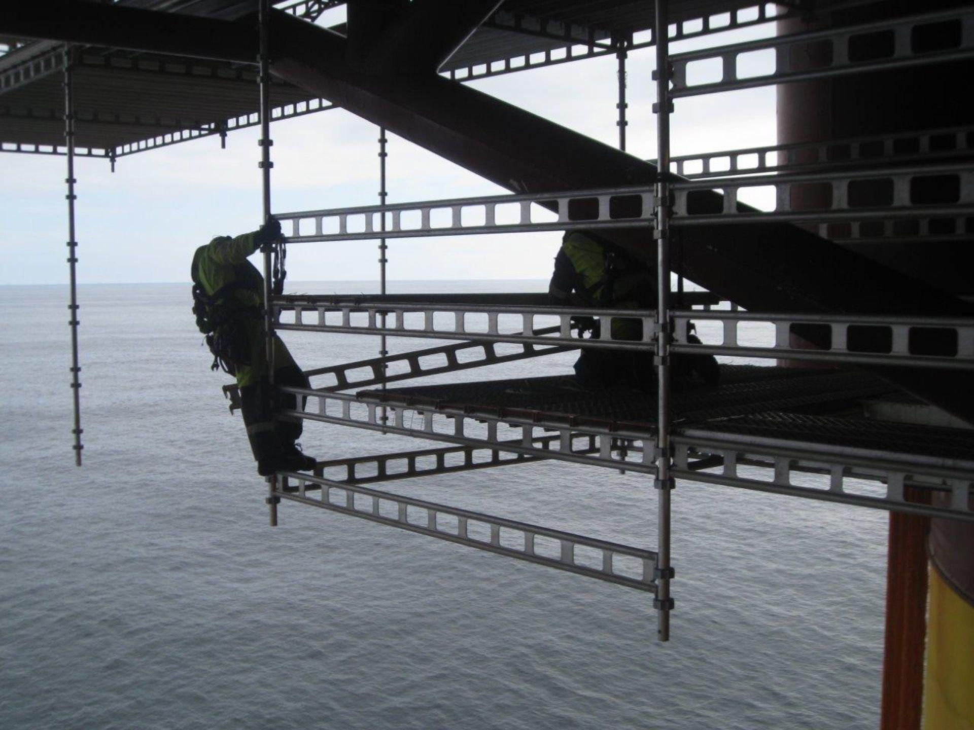 Arbeidere på stillas ved en offshore-plattform, med havet i bakgrunnen. Sikkerhetsutstyr er synlig.