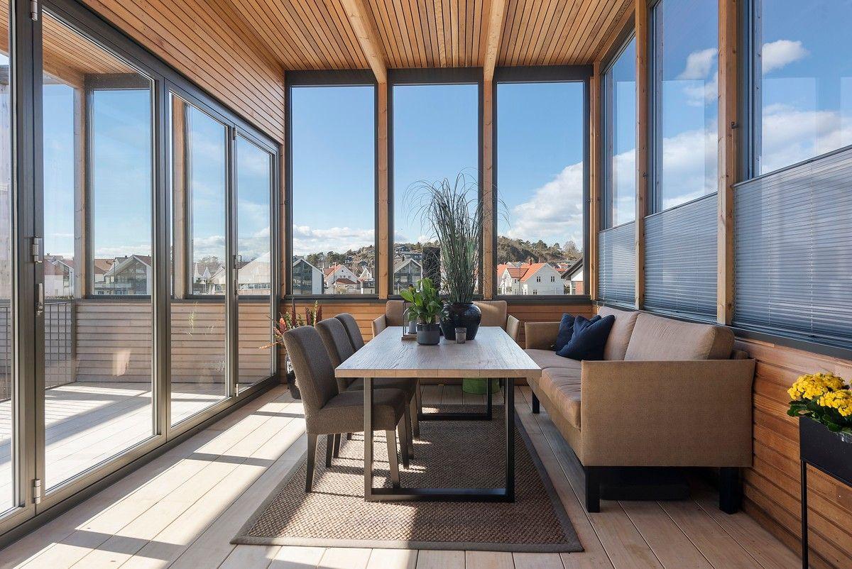 Lys og moderne vinterhage med bord, stoler og sofa, omgitt av store vinduer og utsikt over nabolaget.
