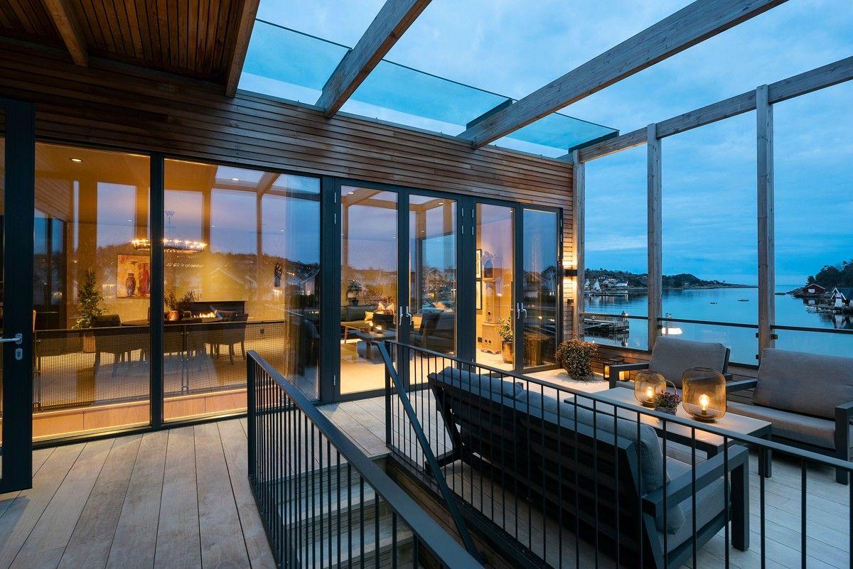 Moderne terrasse med glasstak, utsikt over havet og stilige møbler i kveldslys.