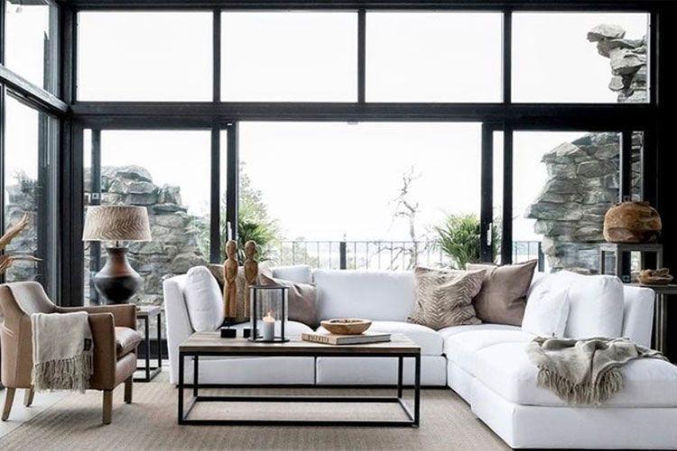 Moderne stue med hvit sofa, brunt lenestol, bord i metall og store vinduer med utsikt mot naturen.