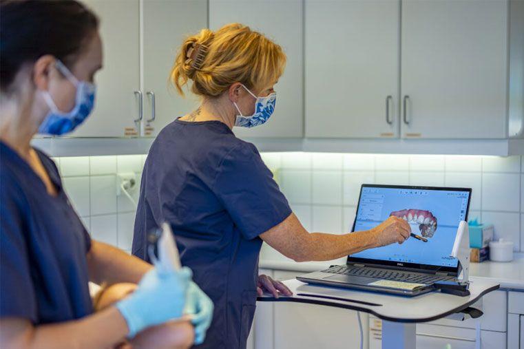 To helsearbeidere i munnhelse, en peker på en dataskjerm med informasjon om tannbehandling.