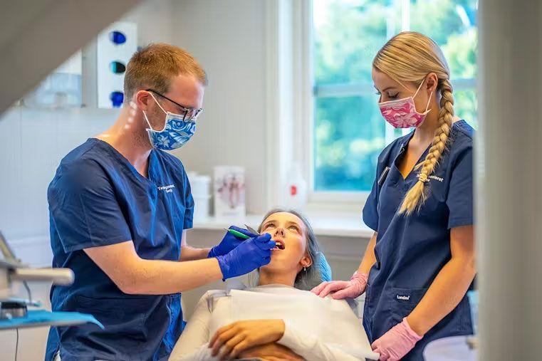 Tannlege og assistent undersøker pasientens tenner i moderne tannlegekontor.