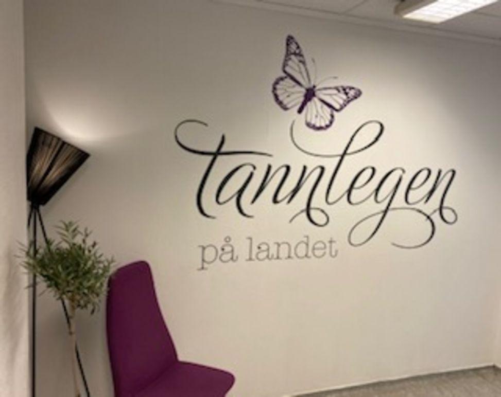 En vegg med teksten "tannlegen på landet" og en sommerfugl, samt en lila stol og en lampe.