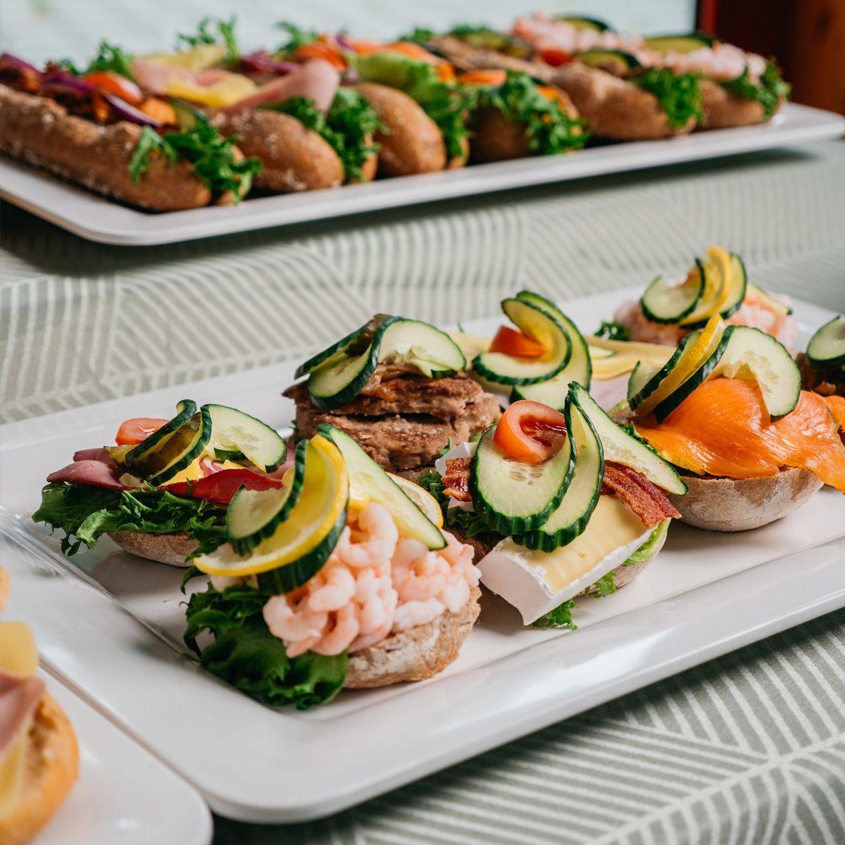 Et fat med smørbrød, inkludert reker, laks, skinke og grønnsaker, ser fristende ut på et bord.
