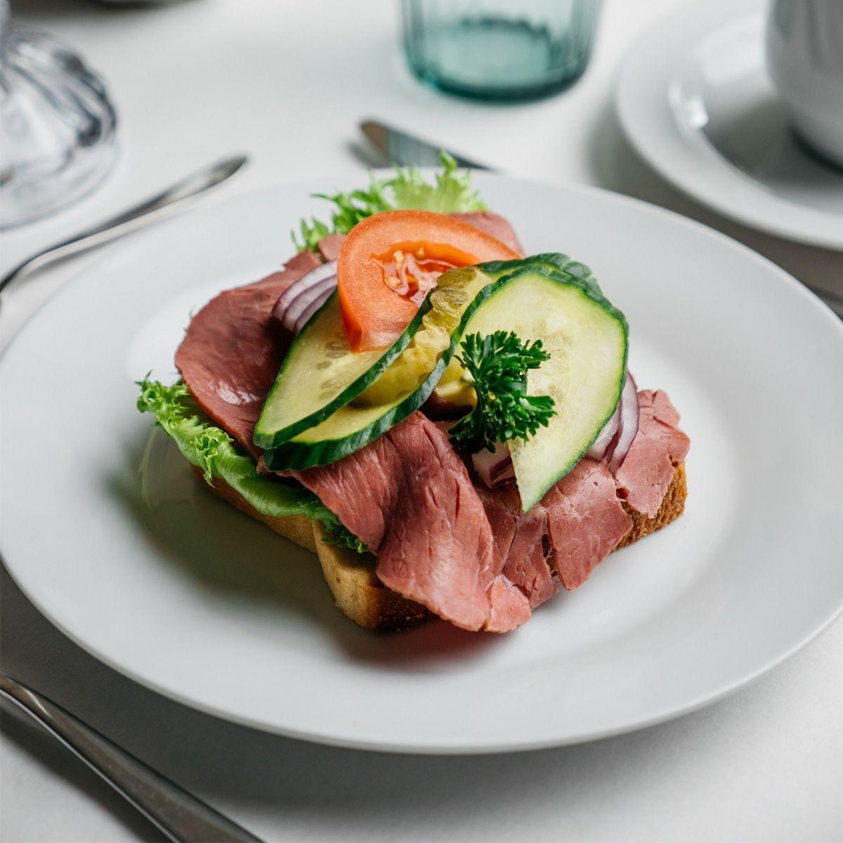 En tallerken med smørbrød toppet med roastbiff, agurk, tomat, løk og salat.