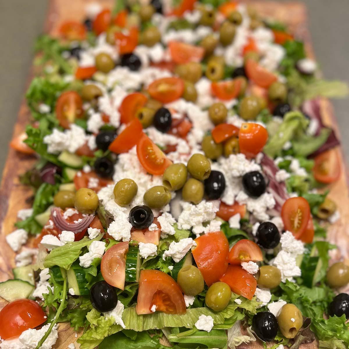 En fargerik salat med grønn salat, cherrytomater, oliven og fetaost på et stort fat.