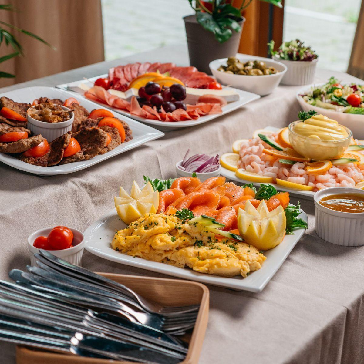 Et variert frokostbord med omelett, frukt, skinke, reker og oliven, dekorert med friske urter.