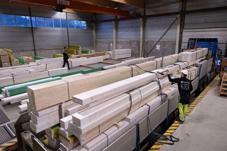 Lager med trelast og ansatte som arbeider med pakking av materialer i en stor bygning.