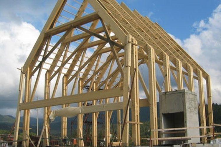 Bygget trehus med synlige bjelker og takstoler under konstruksjon mot en blå himmel.