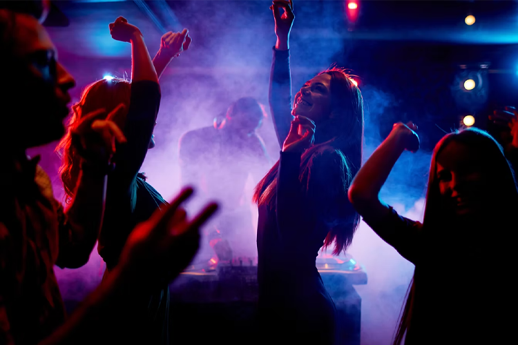 Folk danser og har det moro på en fest med lys og røyk, mens en DJ spiller musikk i bakgrunnen.