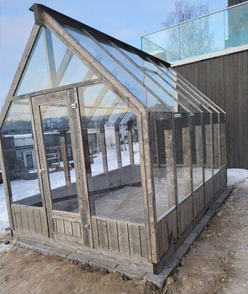 Et moderne drivhus i tre med glassvinduer, plassert på snødekt grunn.