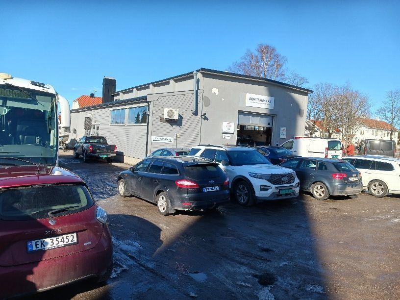 En bilverksted med flere biler parkert foran, under klar blå himmel og sollys.
