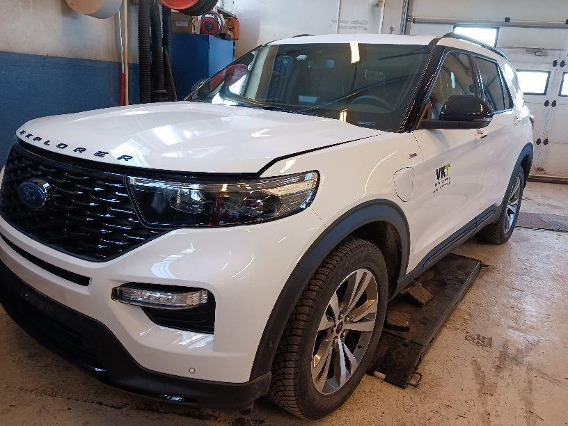 En hvit Ford Explorer SUV står i en verksted med en åpen dør og verktøy i bakgrunnen.