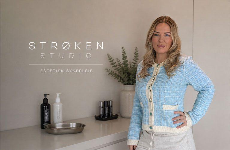 Kvinne i blå genser står foran en moderne frisørsalong med produkter på benken.
