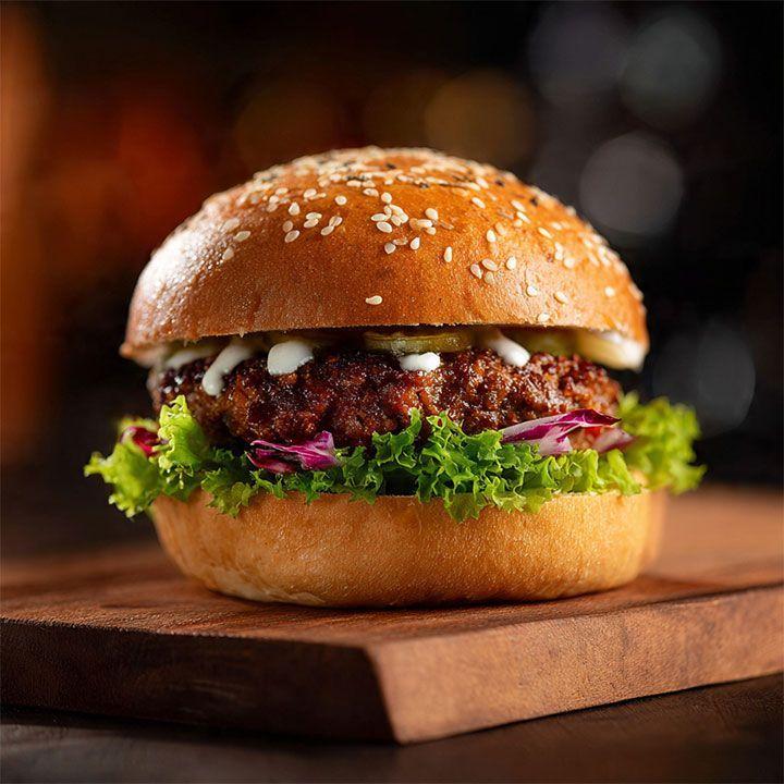 Saftig hamburger med sesambrød, salat, rødkål, agurk og majones på en treplate.