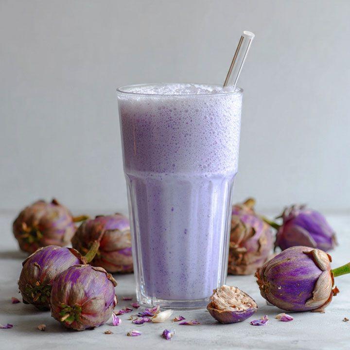 Lilla smoothie i et klart glass med sugerør, omgitt av tørkede blomsterknopper.
