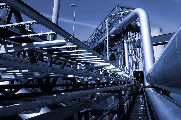Industrielt anlegg med metallrør og strukturer i blått lys, som viser komplekse rørledninger og bygningselementer.