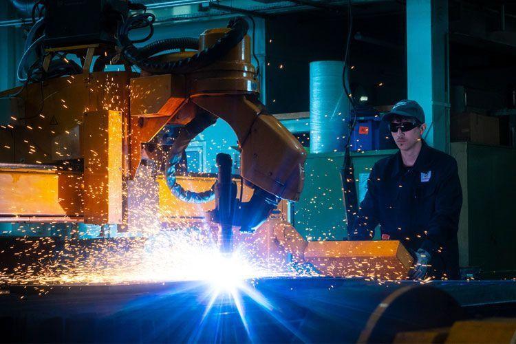 En sveiser jobber med en robotarm som lager gnister i en industriell setting.