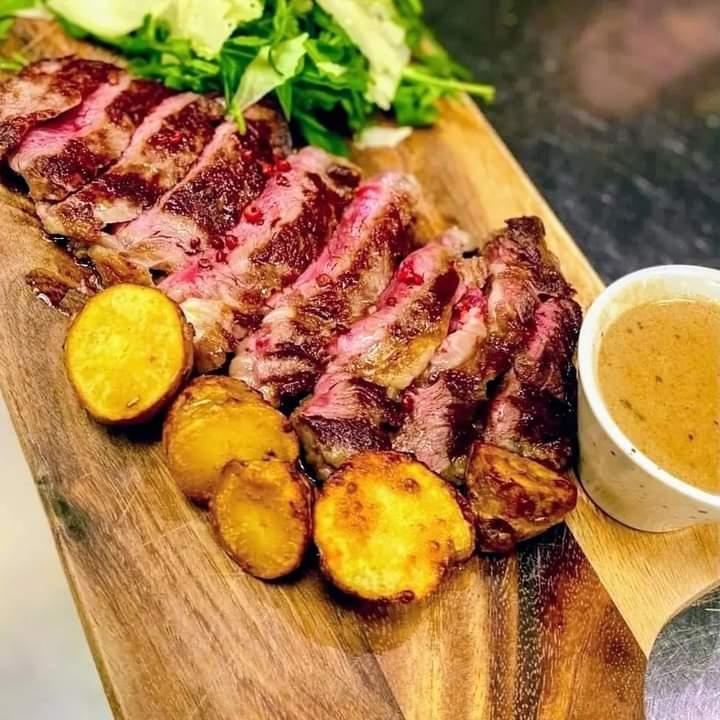 Saftig biffskiver servert med poteter, salat og en liten skål med saus på et trebrett.