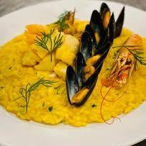 Kremet risotto med reker, blåskjell og poteter, pyntet med dill på en hvit tallerken.
