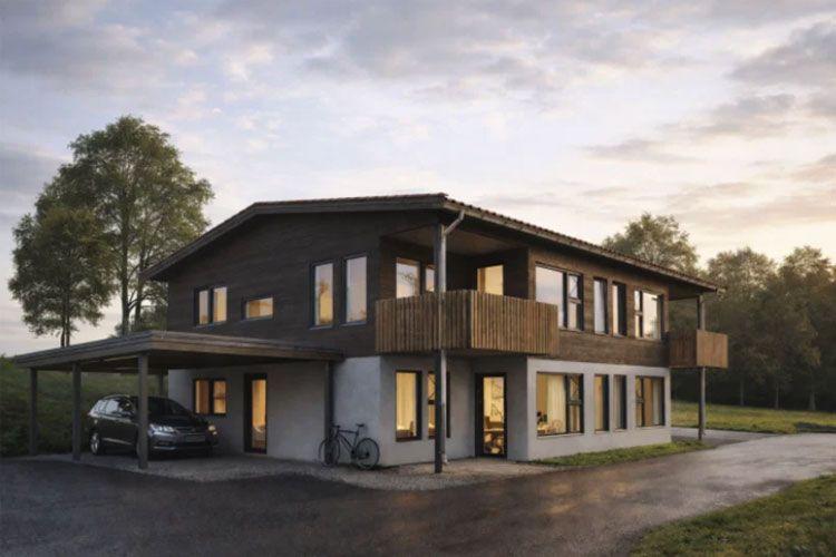 Moderne hus med tre etasjer, balkong og carport, omgitt av trær i solnedgang.