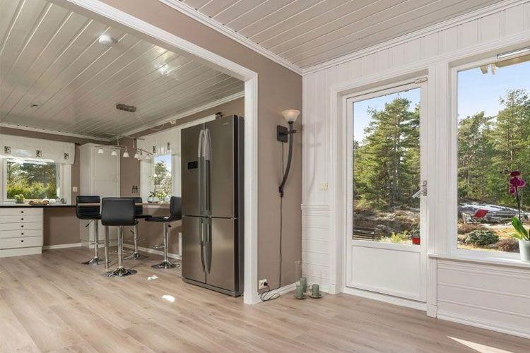 Moderne kjøkken med svart kjøleskap, barstoler og store vinduer som gir naturlig lys. Utsikt mot hagen.
