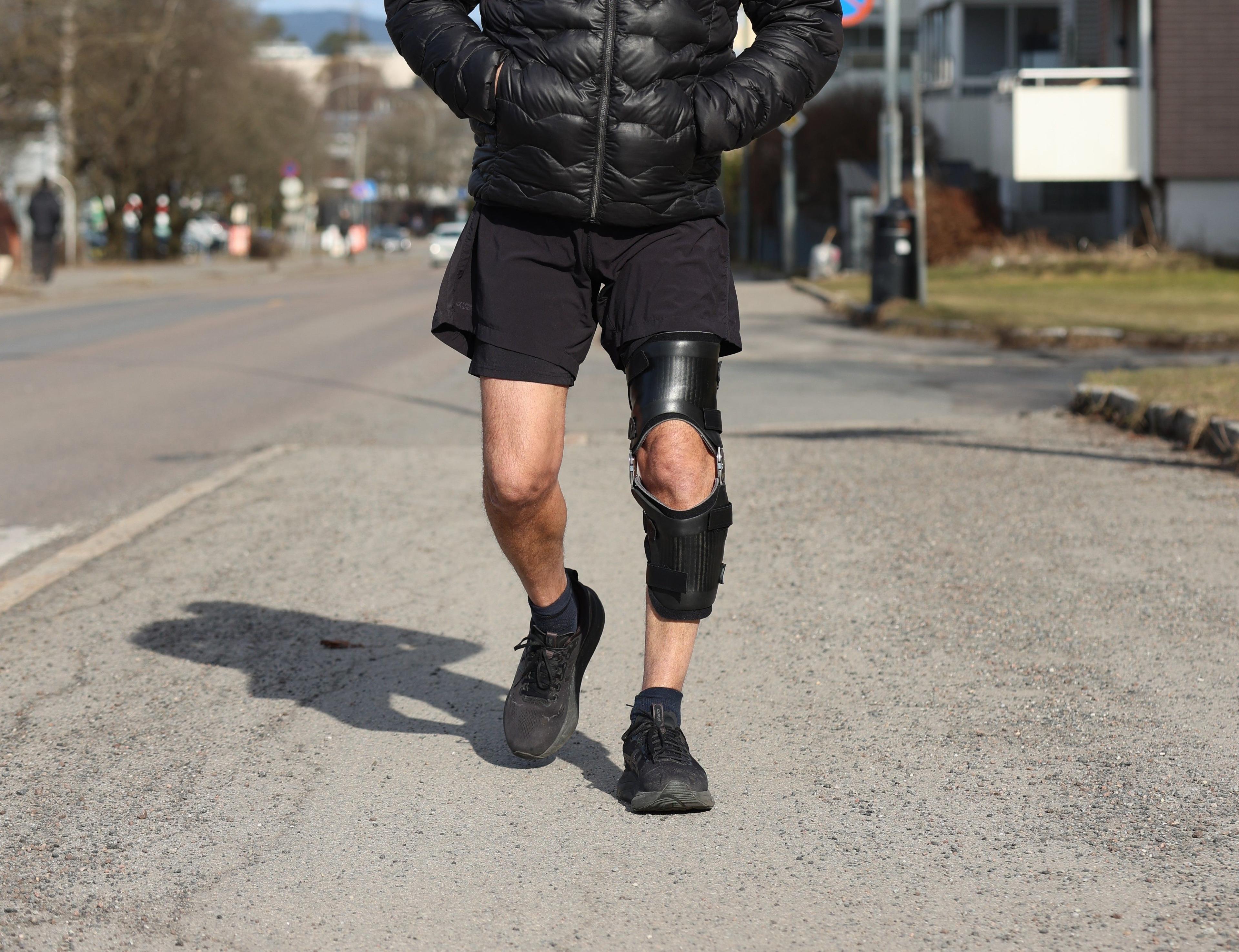 En person jogger på gaten iført shorts og en knebeskytter på det ene benet.