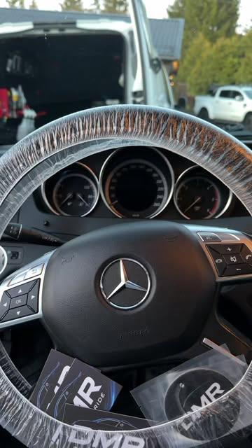 Et nærbilde av et Mercedes-ratt med plastbeskyttelse og instrumentpanel i bakgrunnen.