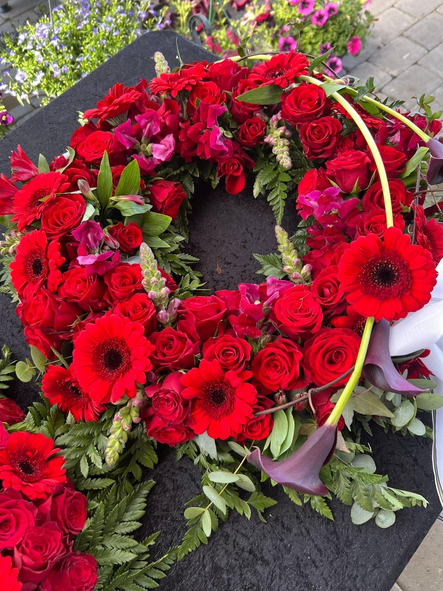 En vakker krans laget av røde roser, gerberaer og grønt, dekorert med lilla blomster.
