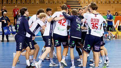 Håndballspillere feirer en seier sammen på banen, iført hvite og mørkeblå drakter.