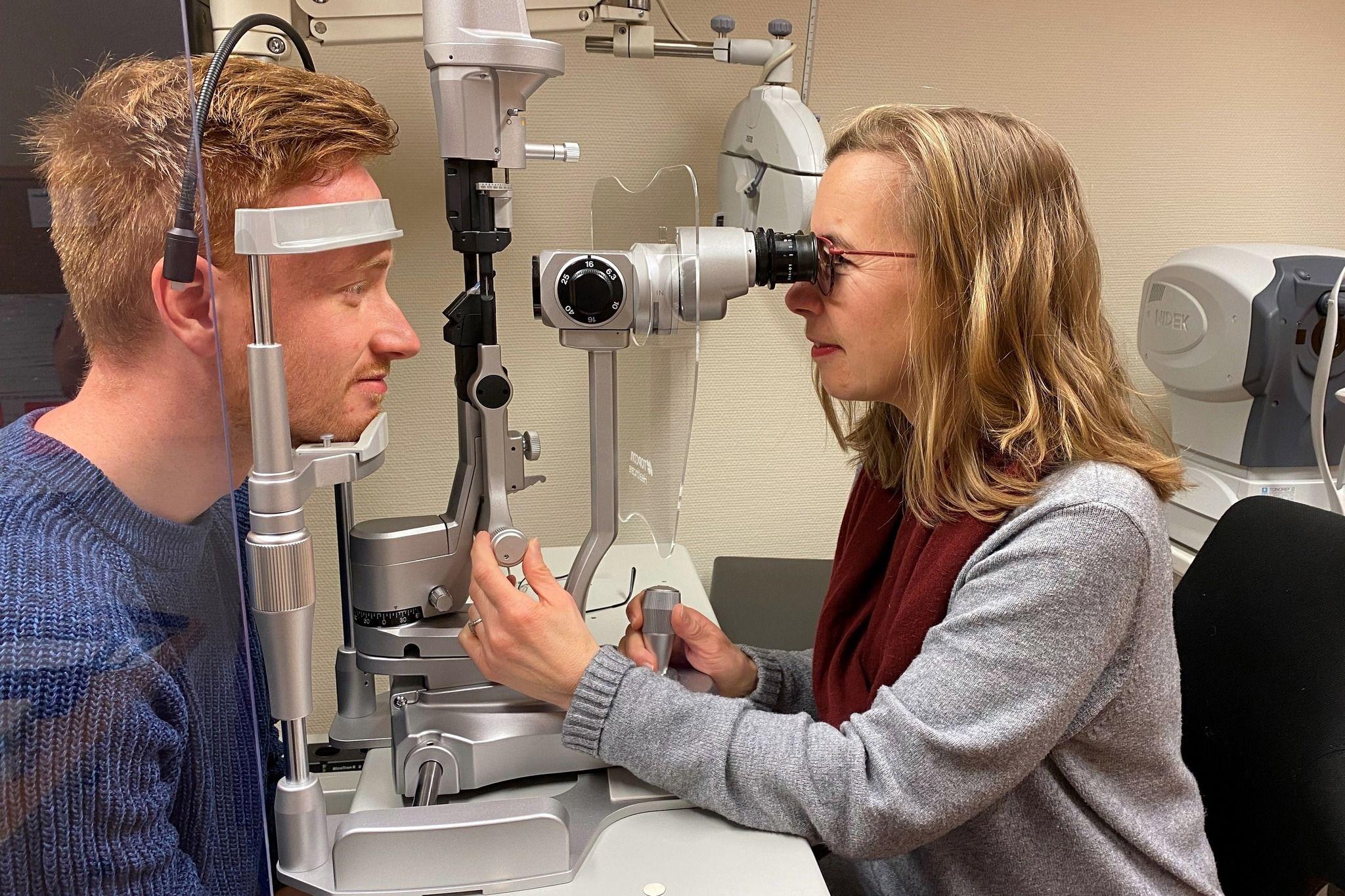 En optiker undersøker en pasients øyne med en spaltelampe i et moderne kontor.