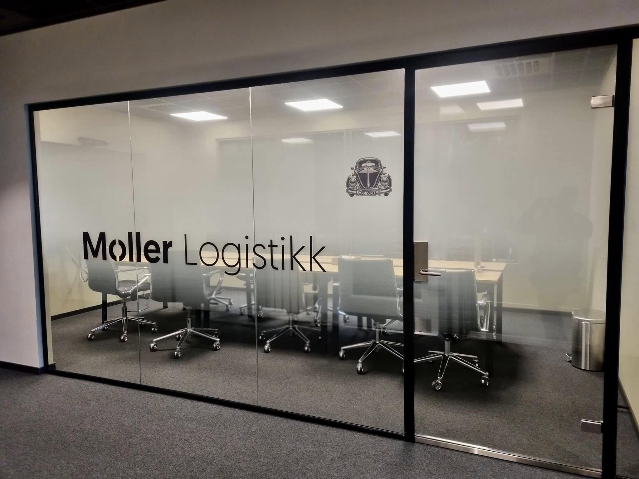 Møterom med glassvegg og bord med stoler, merket med "Moller Logistikk".