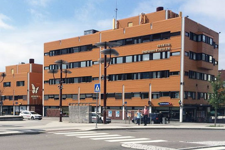 Moderne bygning med tre etasjer, store vinduer og en lys fasade, beliggende ved en gate med fotgjengerovergang.