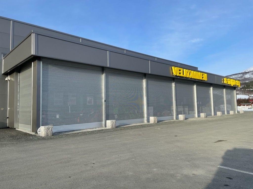 En moderne bygning med rulleporter og skiltet "Welthandler" på fasaden, plassert på en gruslagt parkeringsplass.