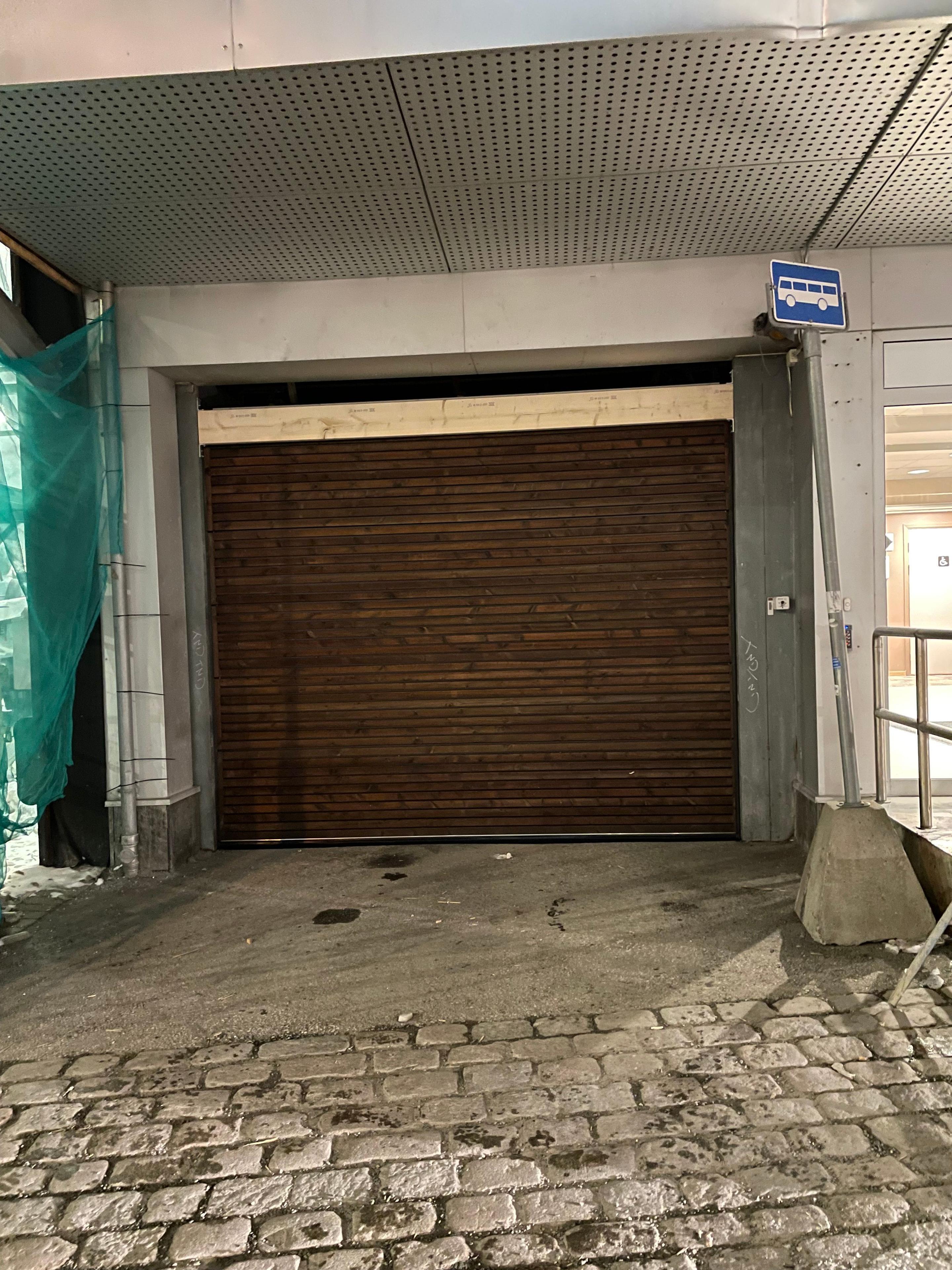 Garasjeport i tre med lukket design, plassert under en bygning med steinlagt fortau.