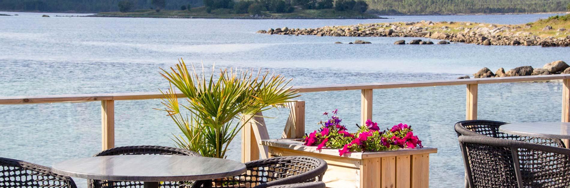 Utsikt over vannet fra en terrasse med blomsterkasser og bord i en koselig restaurant.