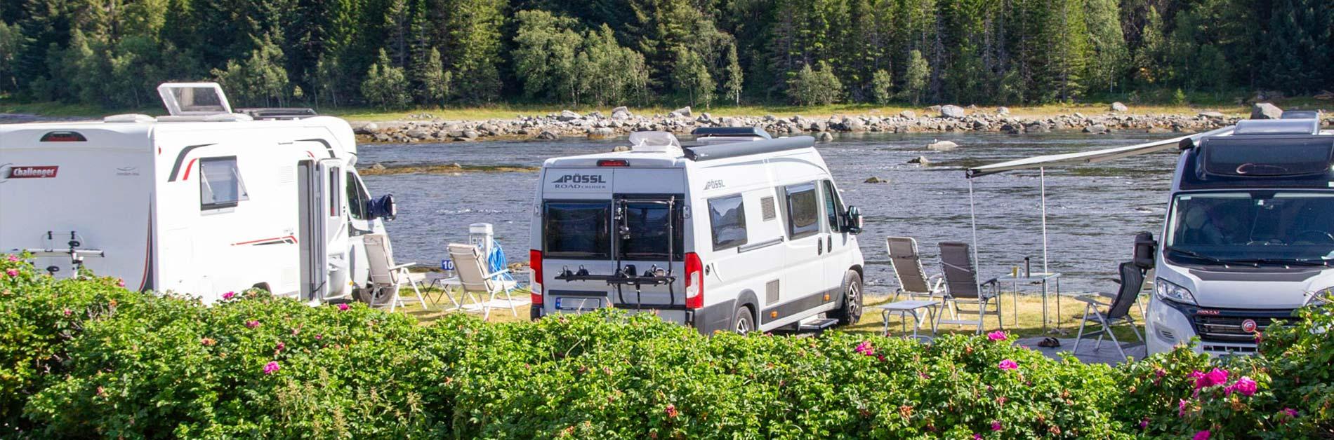 Campingbiler ved elven med stoler og grønt landskap i bakgrunnen.
