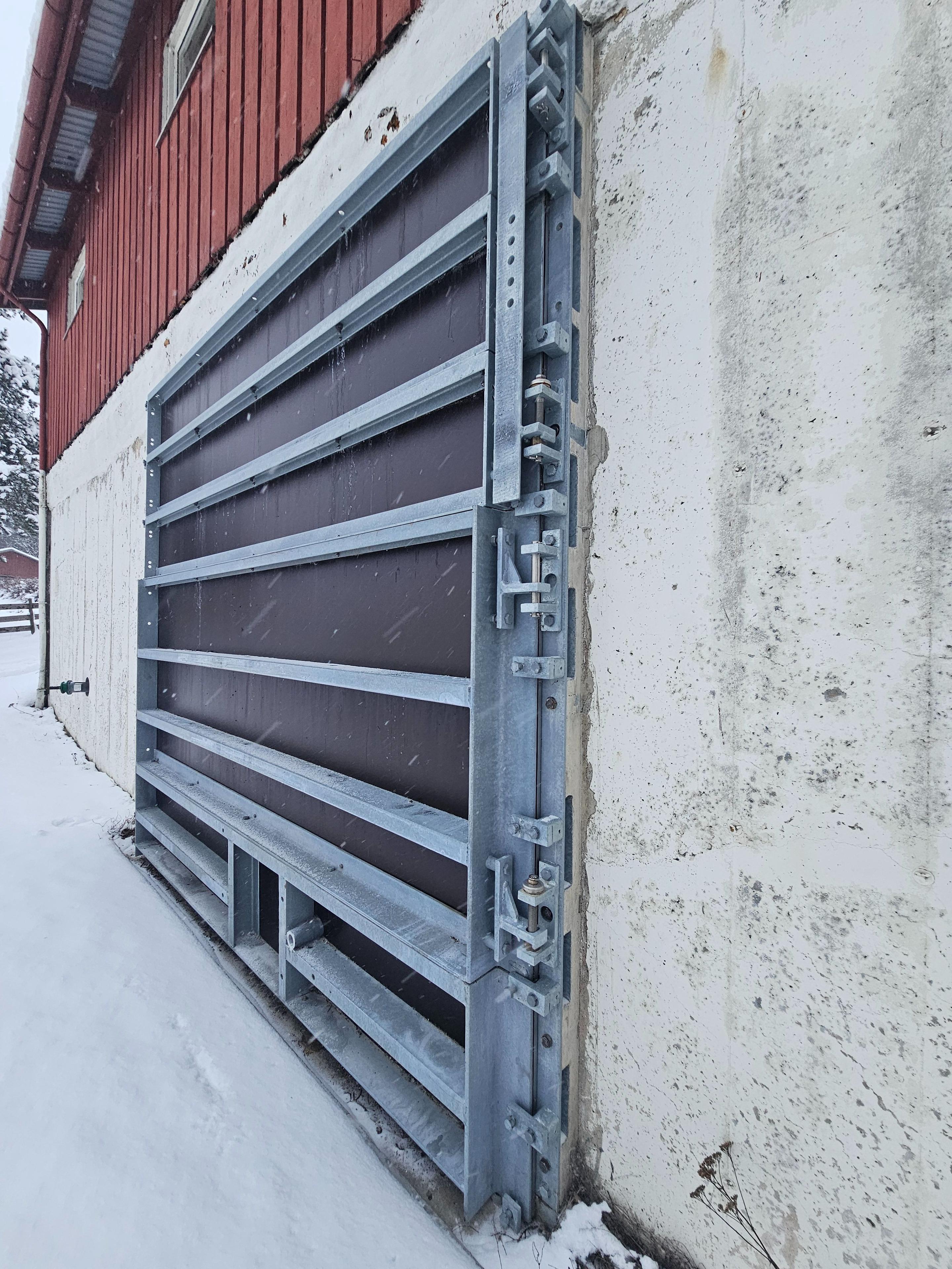 En stor, grå metallport på en vegg av betong, delvis dekket av snø.