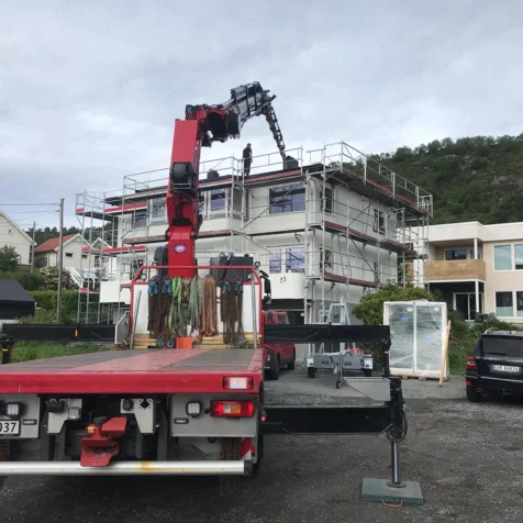 Bygning med stillas og kran, arbeidere på taket, lastebil med utstyr i forgrunnen.