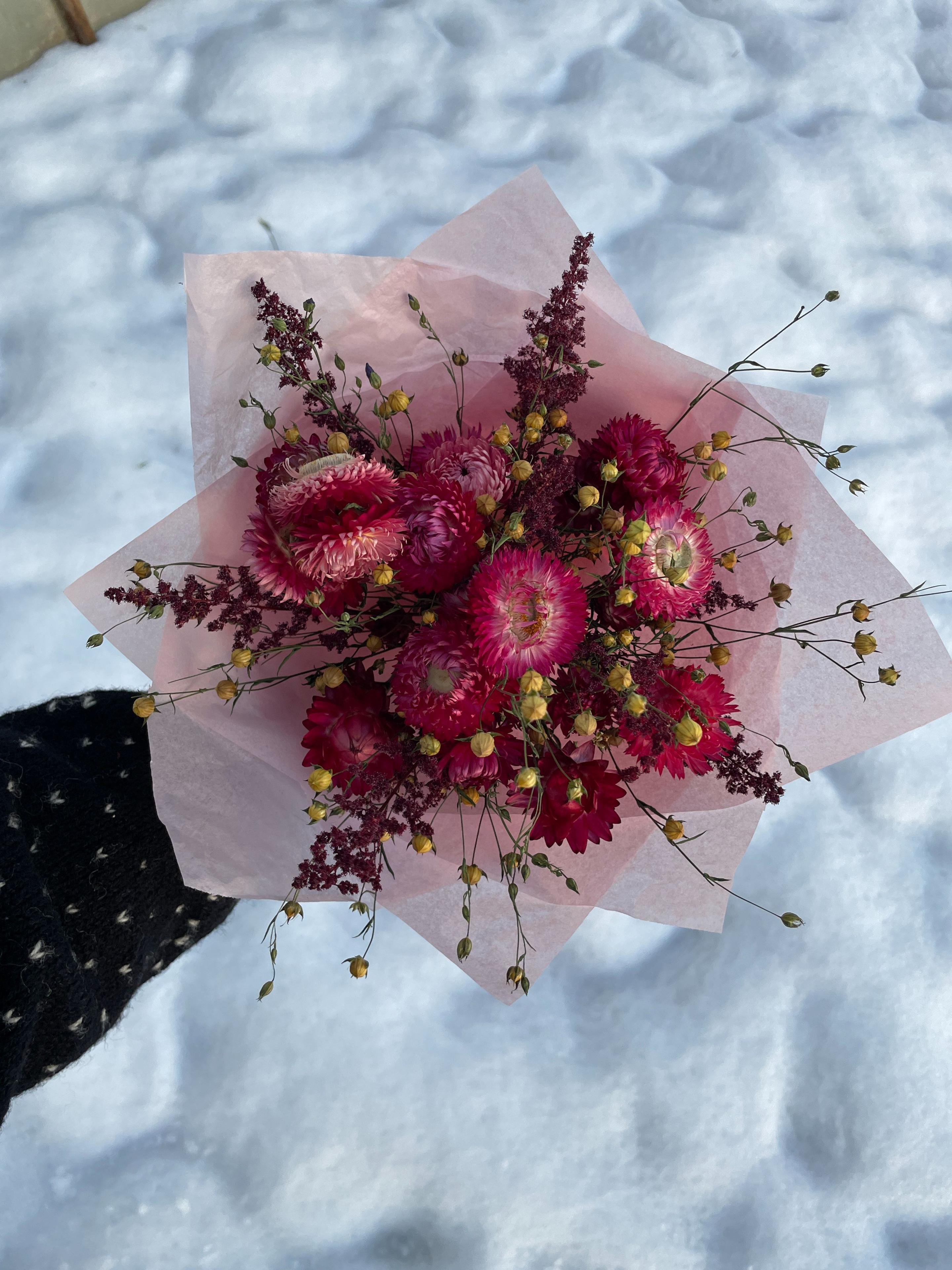 En bukett med rosa blomster og gule detaljer, holdt over snøen.
